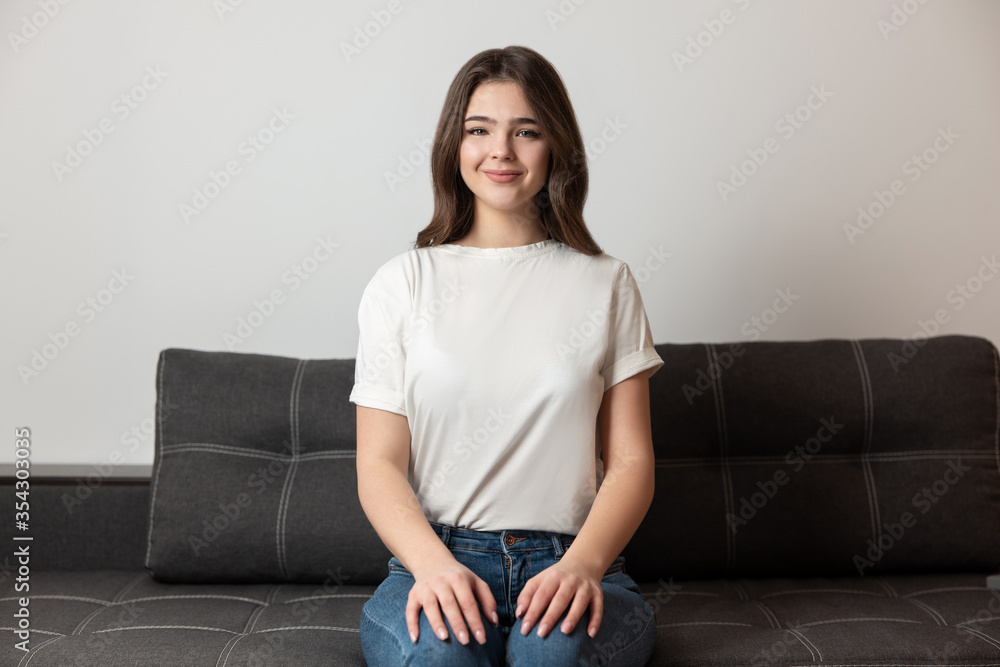 young beautiful brunette woman sitting on the sofa in her appartment holding hands on her legs looking tranquil, feels cozy at home young beautiful brunette woman sitting on the sofa in her appartment holding hands on her legs looking tranquil, feels cozy at home