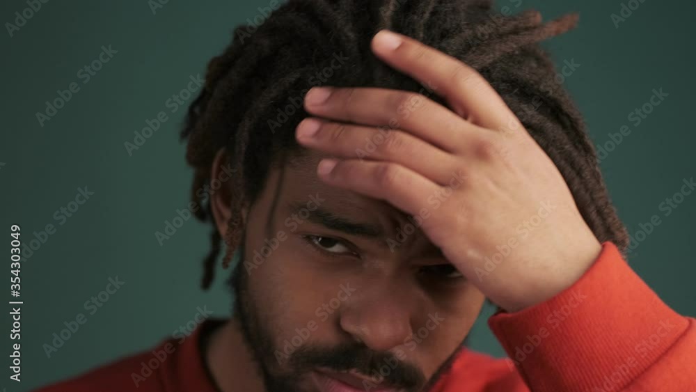 A close-up view of a handsome young african american man is posing to the camera standing isolated over green wall background in studio A close-up view of a handsome young african american man is posing to the camera standing isolated over green wall background in studio