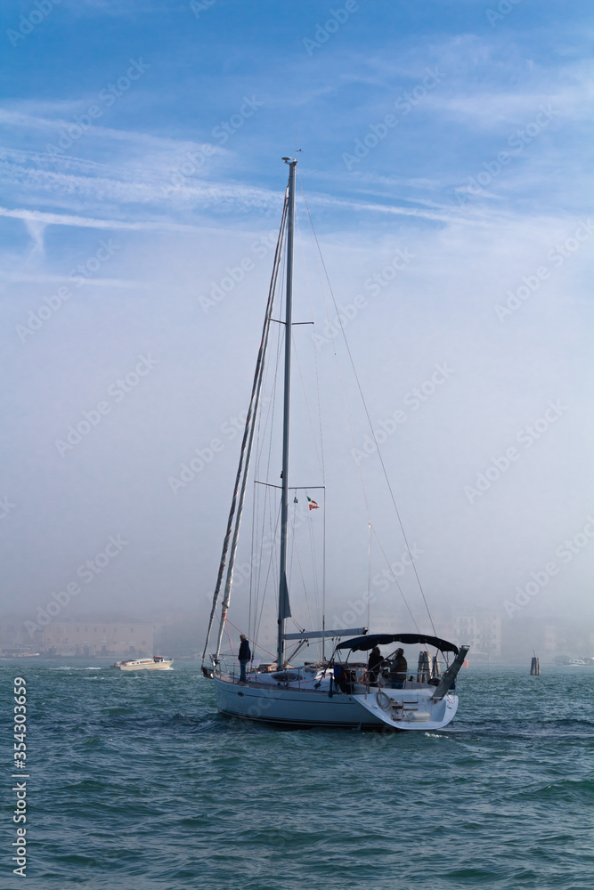 Sailing yacht enters the foggy harbor.