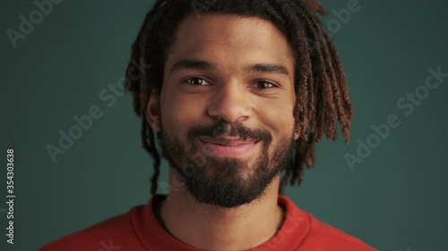 A happy young african american man is winking while standing isolated over green wall background in studio