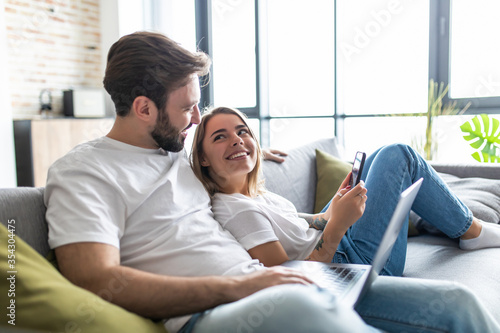 Beautiful young couple relaxing on a couch at home using laptop computer and mobile phone photo