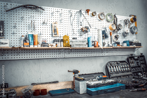 Moto workshop with hand mechanic tools kit. Workbench with sets of keys, screwdrivers, ploskobets, electrical tape, duct tape on wall. Table with motorcycle parts, vise. Workspace for auto mechanic