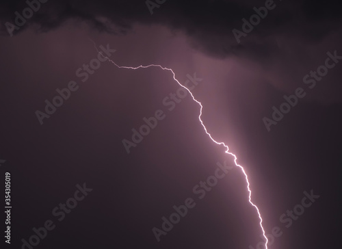 Lightning bolt emerges from dark storm cloud, lighting up night sky