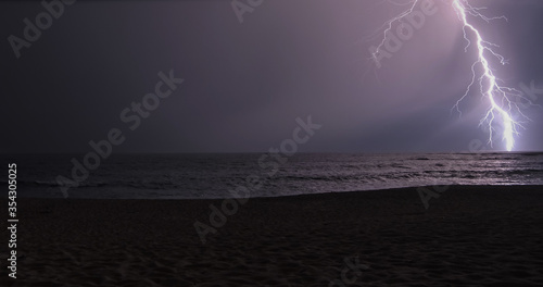 Lightning bolt lights up the sky on beach at night during a storm. Copy space on left.