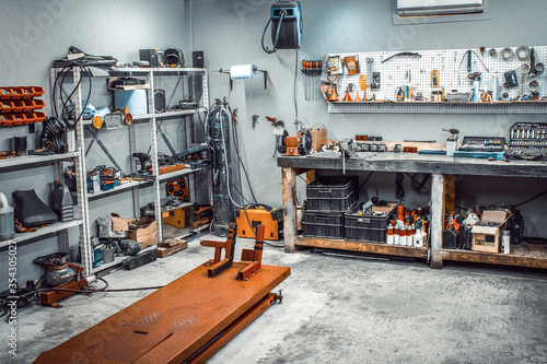 Garage, service area for disassembling, repairing motorcycles, car service station. Inside the workshop with large workbench, shelving, moto lift, tools kit for processing wrenches on the wall