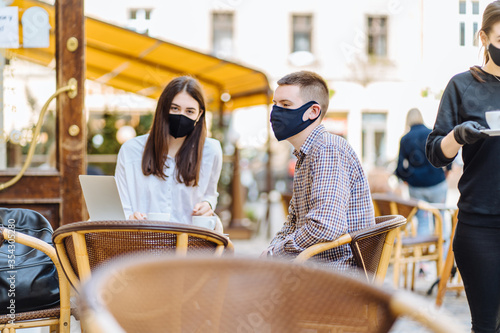 business people in medical masks working with laptop and papers on sunny terrace