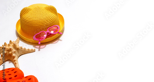 Beach accessories for sun protection: children's yellow straw hat, pink heart-shaped glasses on a white background. Layout with space for text. Ready for travel and beach holidays at sea