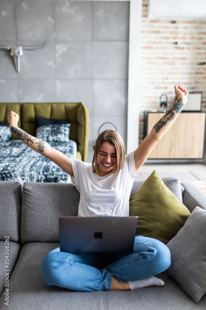 Joyful attractive woman sitting on a white sofa in a home living room ...