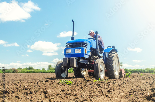 The farmer works on a tractor. Loosening the surface  cultivating the land for further planting. Cultivation technology equipment. Grinding and loosening soil  removing plants roots from last harvest.