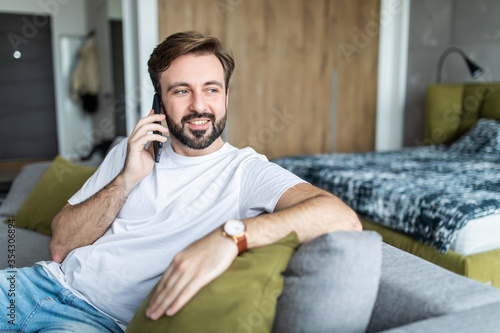 Portrait of cheerful man talking on the phone sitting at couch at home