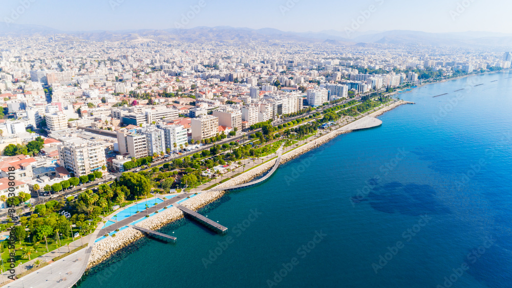 Aerial view of Molos Promenade park on coast of Limassol city centre,Cyprus. Bird's eye view of the jetty, beachfront walk path, palm trees, Mediterranean sea, piers, urban skyline and port from above