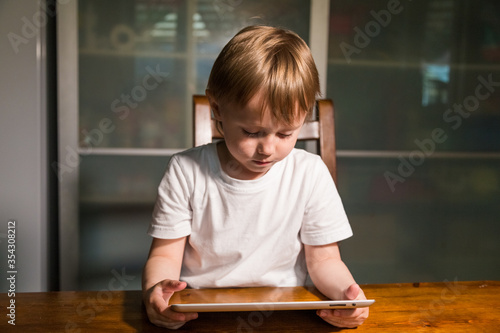 Young girl sitting at the table in the kitchen and watching cartoons on tablet. 