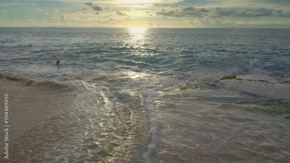 Ocean with big waves during warm sunset and silhouette of youg woman is swomming in dark water with reflections Ocean with big waves during warm sunset and silhouette of youg woman is swomming in dark water with reflections