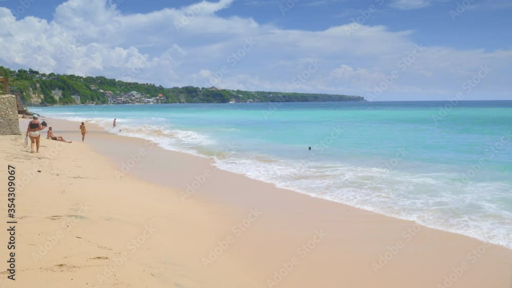 People are walking, relaxing and swimming on tropical beach with big foamy waves and bright blue water in hot sunny day People are walking, relaxing and swimming on tropical beach with big foamy waves and bright blue water in hot sunny day