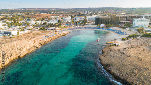 Aerial bird's eye view of Vathia Gonia beach, Ayia Napa, Famagusta, Cyprus. The landmark tourist attraction rocky bay at sunrise with golden sand, sunbeds, sea restaurants in Agia Napa, from above.