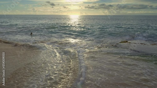 Ocean with big waves during warm sunset and silhouette of youg woman is swomming in dark water with reflections photo