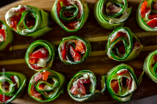 Cucumber rolls with sweet pepper and white cream cheese served on wooden plate.Green rolls with tomato and cream cheese on wooden background.Cucumber canape with smoked salmon and herb cream cheese.