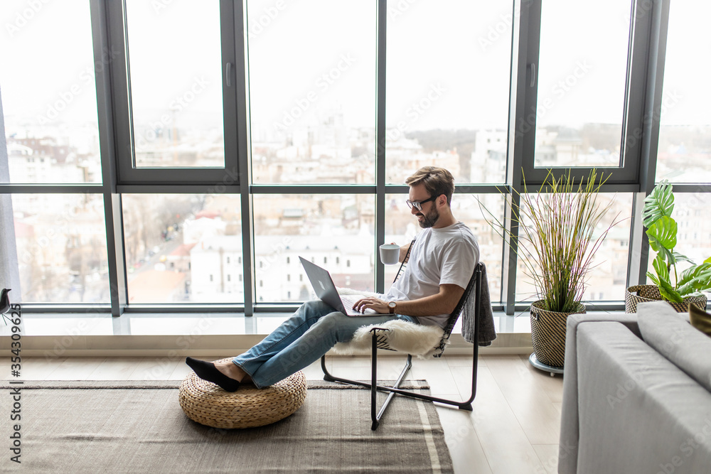 Portrait of a smiling man relaxing on chair near window ise laptop