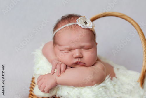 Close-up of an adorable newborn baby sleeping in a wicker basket. Sweet baby lies in a basket and smiles in his sleep. Isolated on a white background Studio. Sleeping girl with a flower on her head.