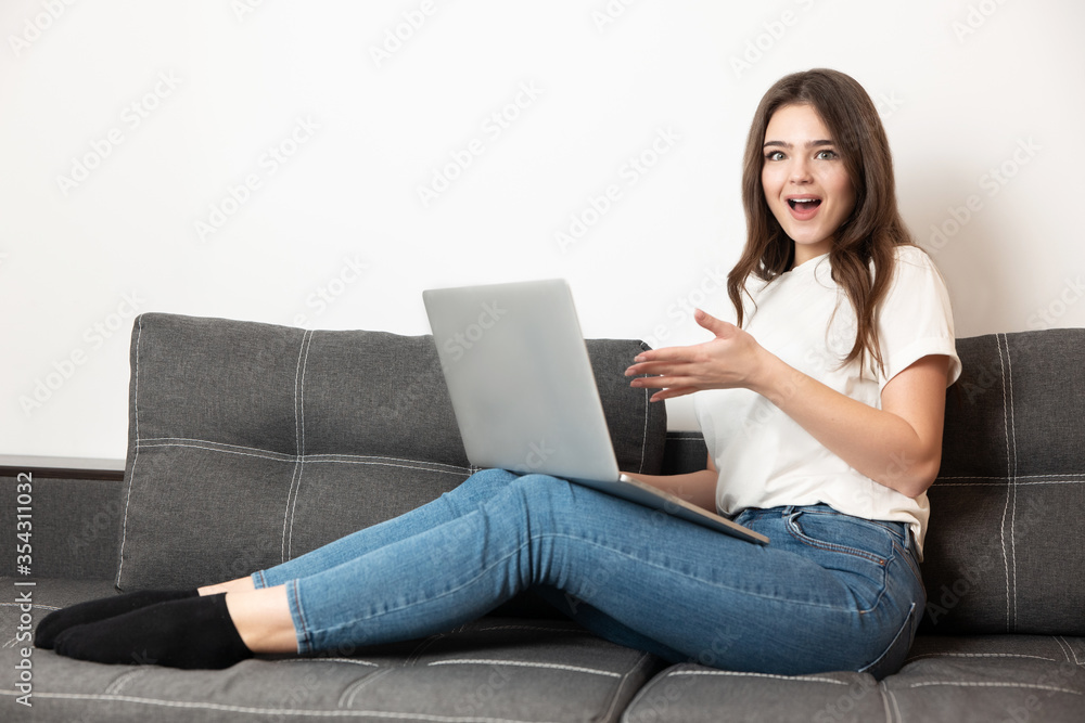 young beautiful woman working from home in her laptop sitting on the sofa in her appartment during quarantine isolation looks surprised, stay safe home concept young beautiful woman working from home in her laptop sitting on the sofa in her appartment during quarantine isolation looks surprised, stay safe home concept