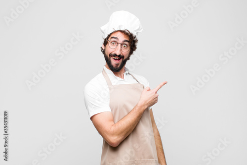 young crazy chef looking excited and surprised pointing to the side and upwards to copy space against white wall