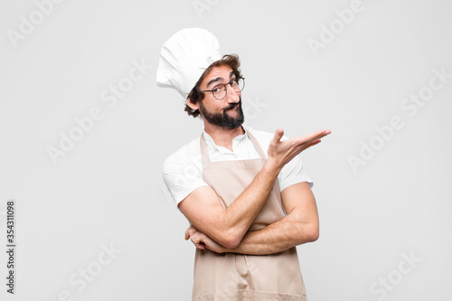 young crazy chef feeling confused and clueless, wondering about a doubtful explanation or thought against white wall photo