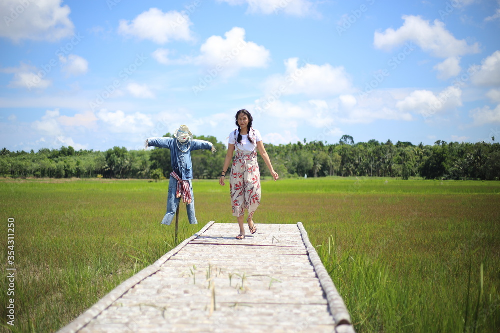 A woman standing on a wooden bridge in a rice field A woman standing on a wooden bridge in a rice field