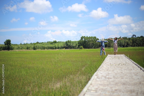 A woman standing on a wooden bridge in a rice field