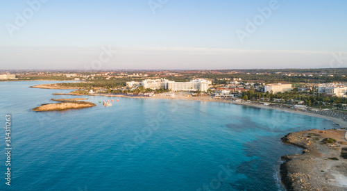Aerial bird's eye view of famous Nissi beach coastline, Ayia Napa, Famagusta, Cyprus.Landmark tourist attraction islet bay at sunrise with golden sand, sunbeds, sea restaurants in Agia Napa from above © f8grapher
