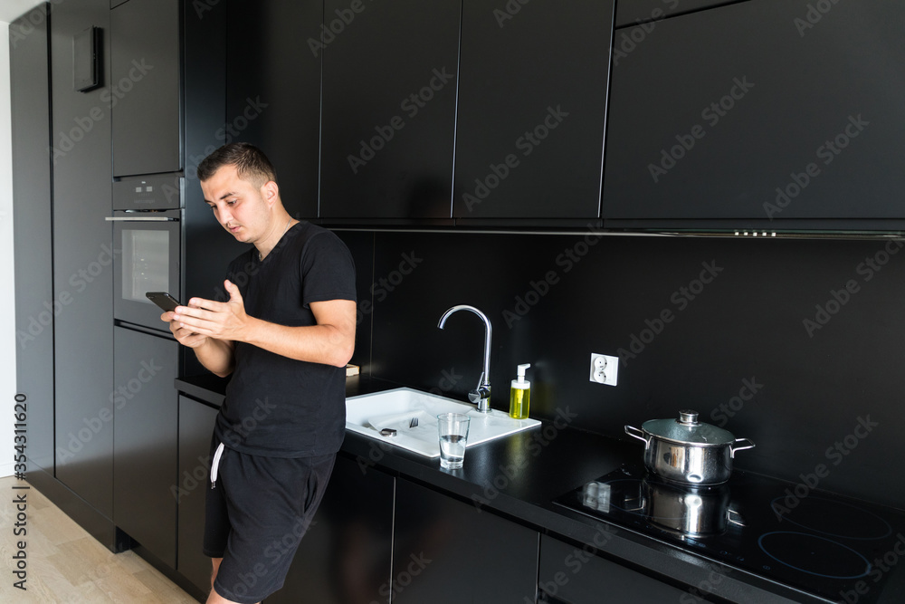 Smiling young man use cellphone gadget texting messaging standing in kitchen