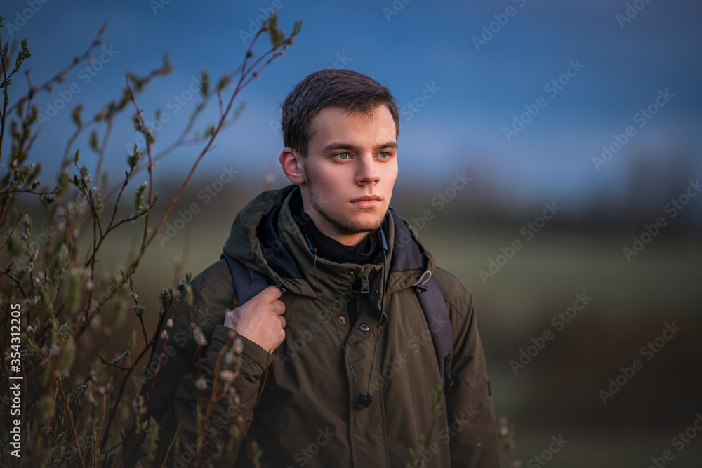 portrait of a guy with a backpack on nature against the evening sky	