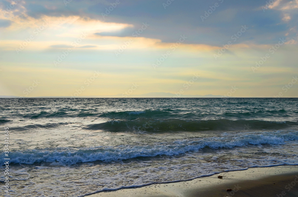 Gentle waves on a sandy beach with cloudy  deep blue sky  in summer evening 