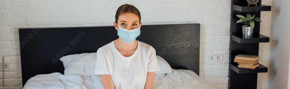 Panoramic crop of young woman in medical mask looking at camera on bed Panoramic crop of young woman in medical mask looking at camera on bed