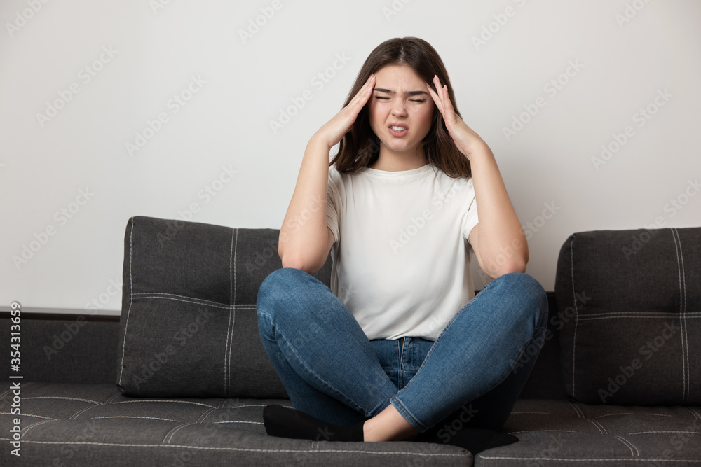 young beautiful brunette woman sitting on the sofa suffering from extreme headache looking desperate, healthcare and medical concept young beautiful brunette woman sitting on the sofa suffering from extreme headache looking desperate, healthcare and medical concept