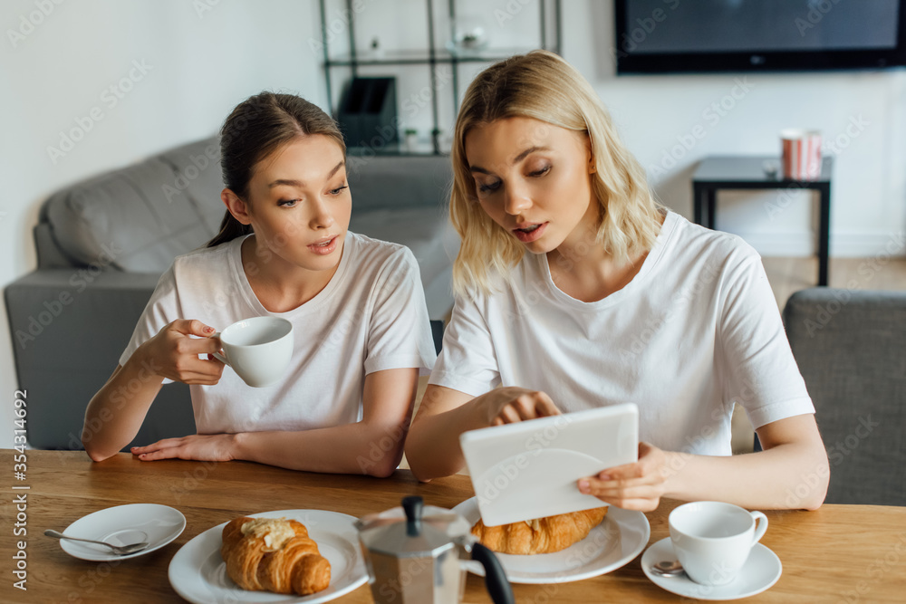 Selective focus of sisters using digital tablet during breakfast in kitchen Selective focus of sisters using digital tablet during breakfast in kitchen