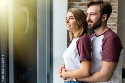 Fototapeta Naklejka Na Ścianę i Meble -  Young guy embracing his girlfriend and both looking through window