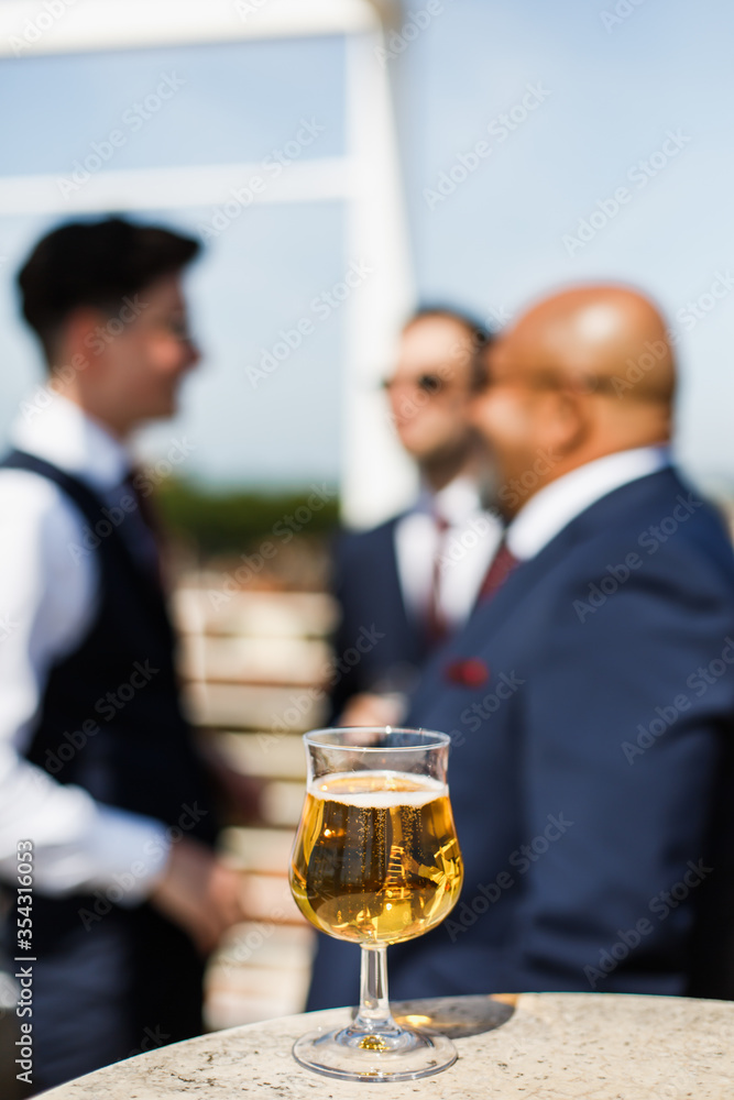 Glass of beer on the table. In the background, three men in suits communicate with each other. Soft focus