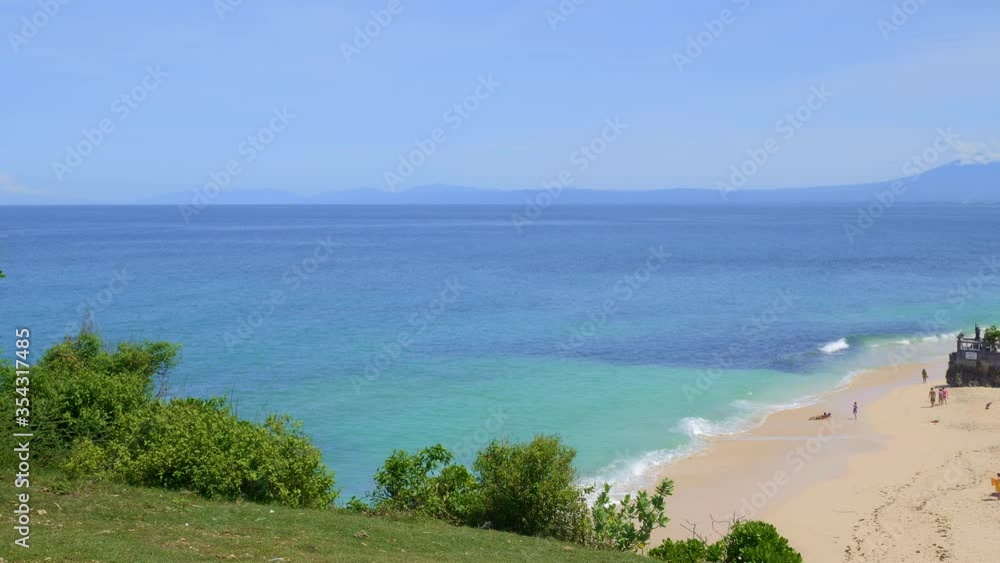 Panorama of a beach on tropical island with bright blue water and waves from green hill Panorama of a beach on tropical island with bright blue water and waves from green hill