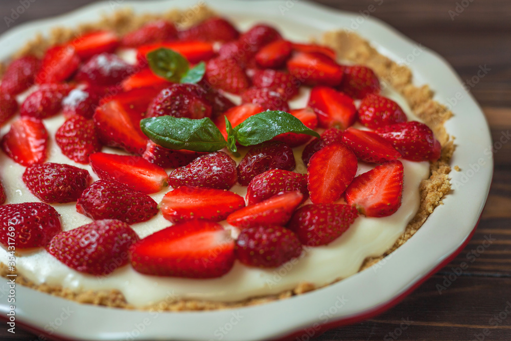 Strawberry cheesecake with basil leaves, in a red ceramic baking dish on a wooden background. Selective focus Strawberry cheesecake with basil leaves, in a red ceramic baking dish on a wooden background. Selective focus
