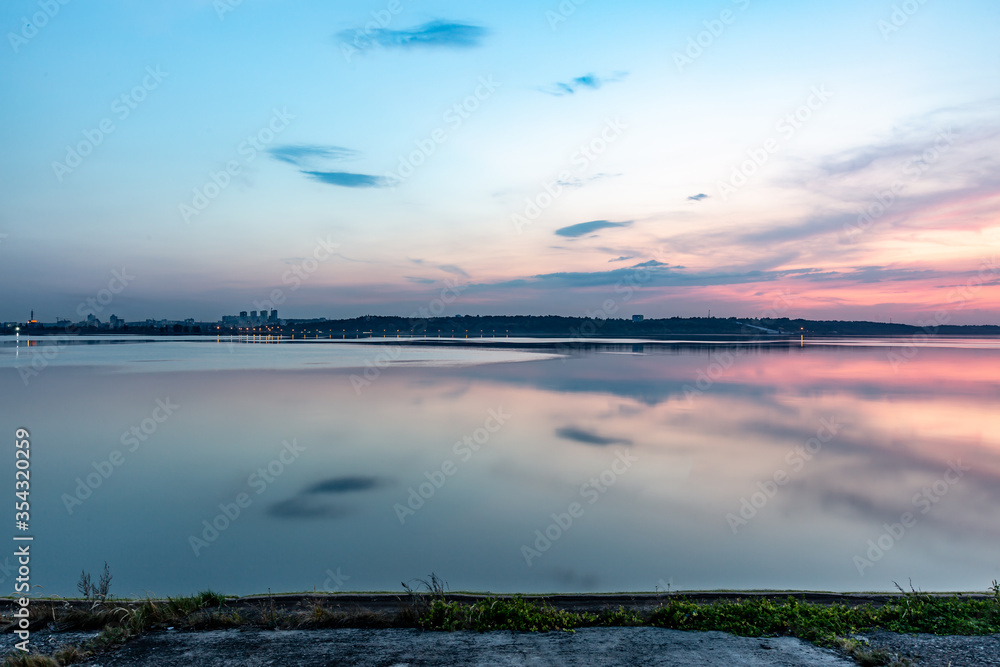 Sunset over the river reservoir sea in pink and blue shades. View of the opposite shore. Horizontal orientation. 