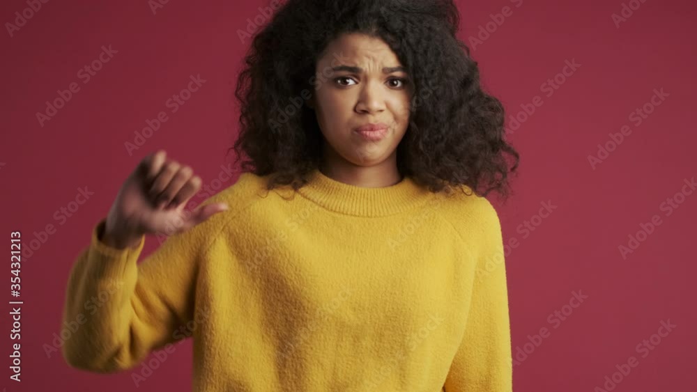 Young negative african woman isolated over dark red burgundy background showing thumbs down gesture Young negative african woman isolated over dark red burgundy background showing thumbs down gesture