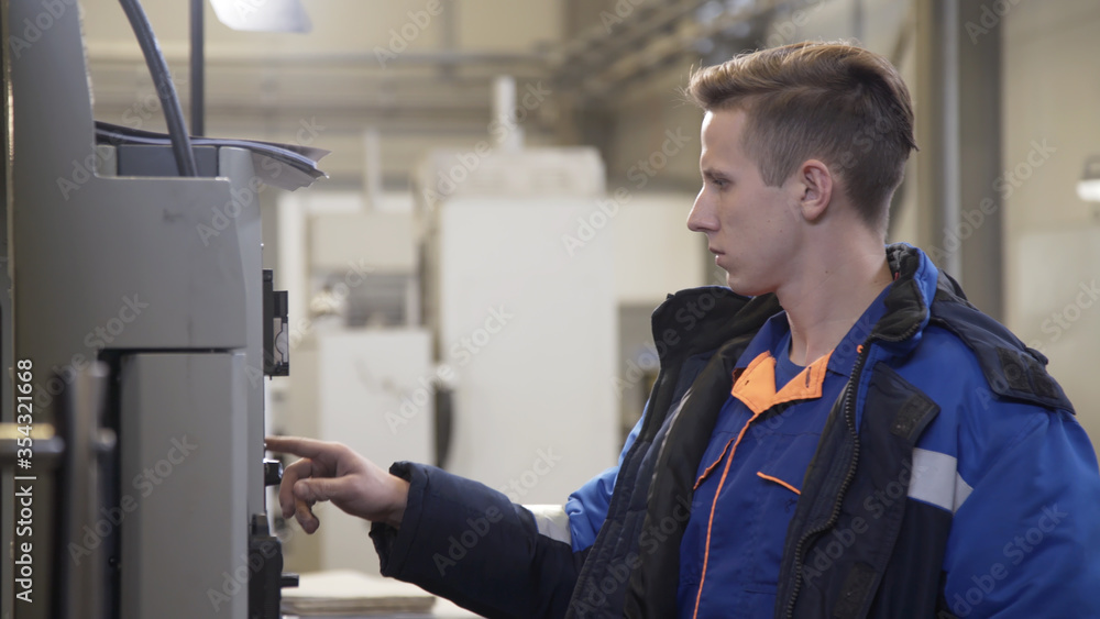 Young male operator of CNC milling machine stands at control panel in the workshop. High precision CNC machining center working, operator machining metal blank process in industrial factory Young male operator of CNC milling machine stands at control panel in the workshop. High precision CNC machining center working, operator machining metal blank process in industrial factory