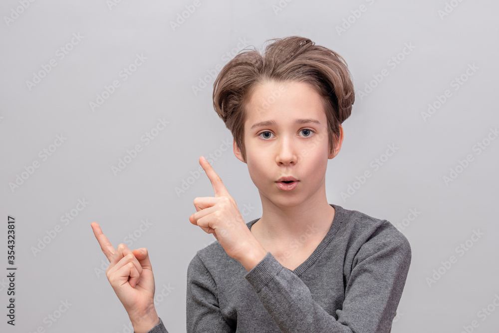 Obraz premium Emotional portrait of a boy closeup, a teenager shows up on gray background, his mouth open in amazement