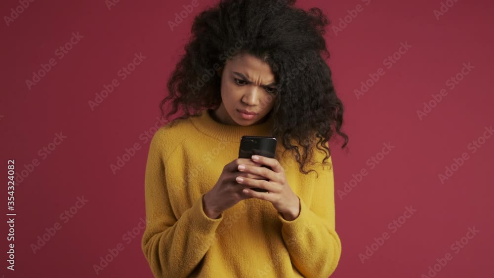 Young african displeased woman isolated over dark red burgundy background using mobile phone Young african displeased woman isolated over dark red burgundy background using mobile phone