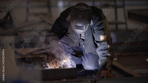 Blacksmith welder in protective mask works with metal steel and iron using welding machine, bright sparks and flashes. Welder uses mask to protect eyes from spark. Professional industry welder working