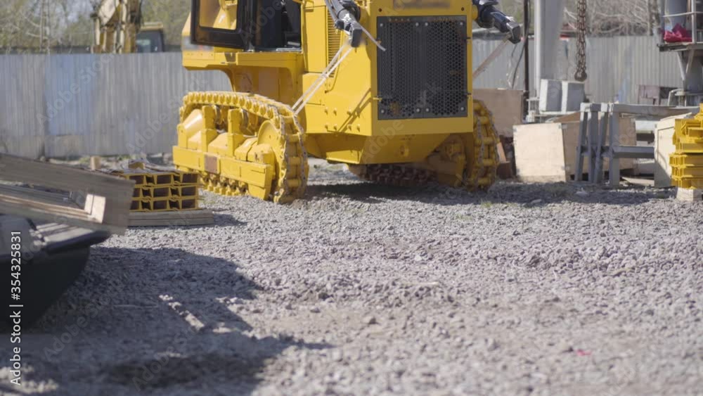 Yellow tracked tractor riding outdoors at plant. Vehicle working at factory on sunny day. Manufacture, industry, heavy equipment, business. Yellow tracked tractor riding outdoors at plant. Vehicle working at factory on sunny day. Manufacture, industry, heavy equipment, business.