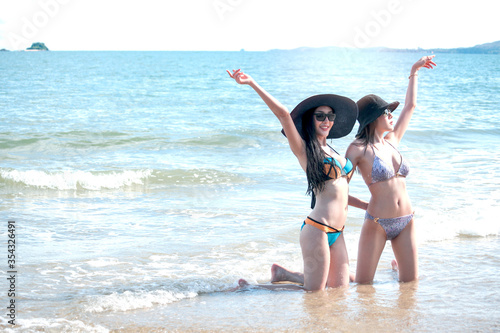 Happy summer holiday vacation, hot sexy beautiful two women in bikini and hat having fun on the beach together, resting and spending time with friend to relexation on tropical island with blue sae