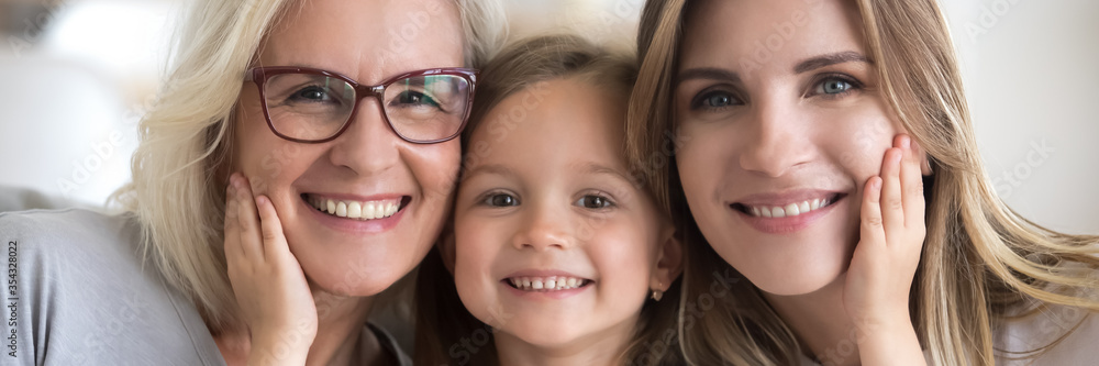 Little girl her young mother and mature grandma portrait. Multi generational women faces smiling looking at camera close up view photo, family bond concept. Horizontal banner for website header design Little girl her young mother and mature grandma portrait. Multi generational women faces smiling looking at camera close up view photo, family bond concept. Horizontal banner for website header design