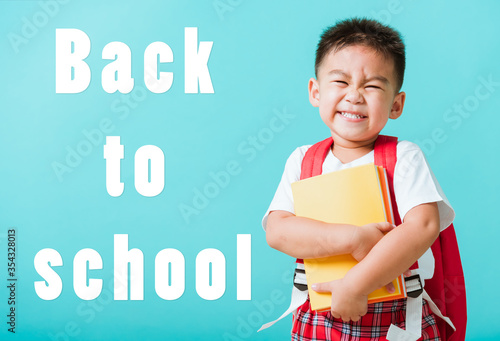 Back to school concept. Portrait Asian happy funny cute little child boy smiling and laugh hug books  studio shot isolated blue background. Kid from preschool kindergarten with school bag education