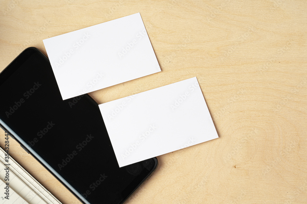 Fototapeta premium Mock up of blank business card and black smartphone screen on table